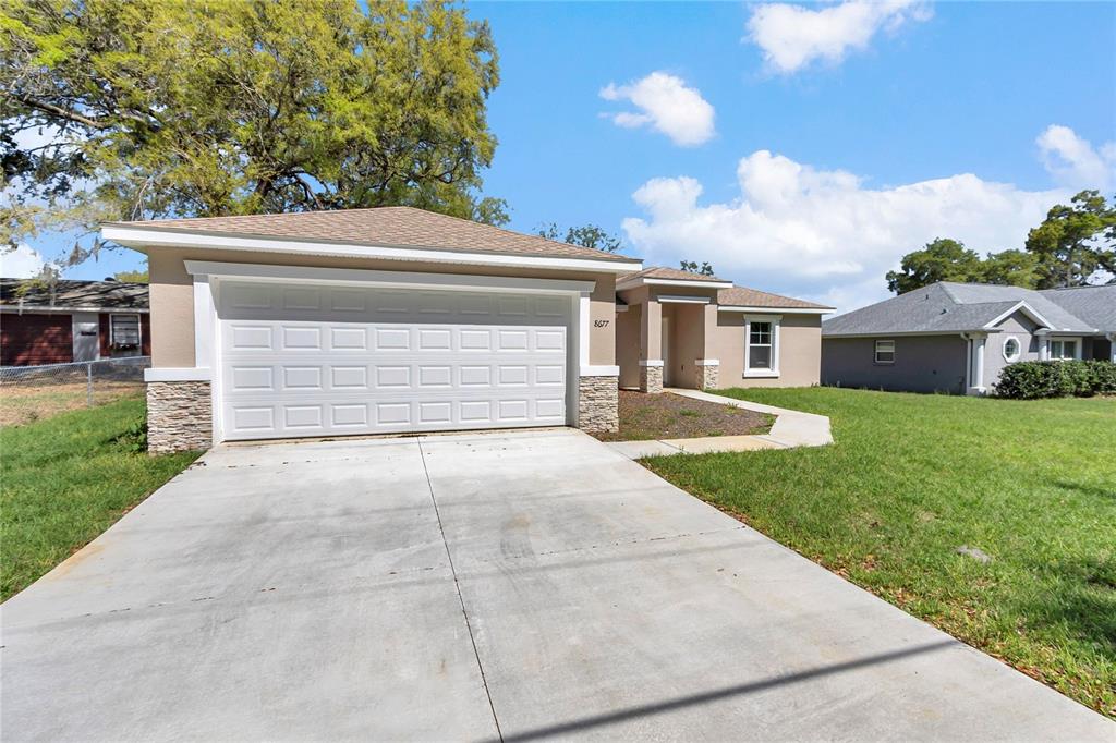A beige single-story house with a white garage door and a stone-accented exterior — 8677 SE 157TH PLACE, SUMMERFIELD, FL