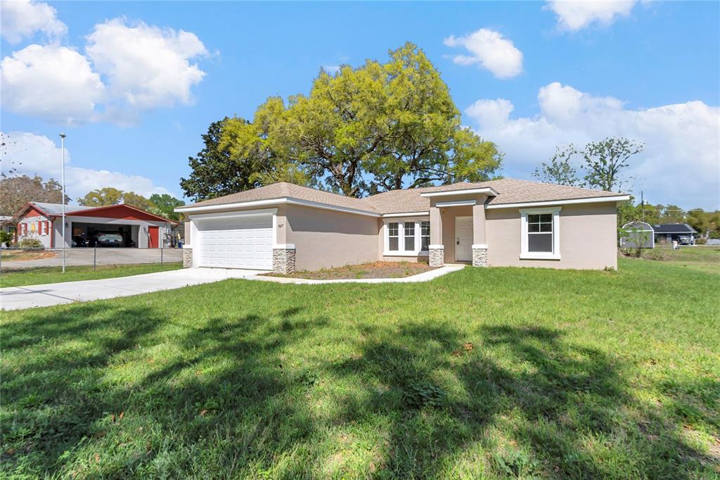 A single-story house with a beige stucco exterior, stone accents, and a two-car garage — 8677 SE 157TH PLACE, SUMMERFIELD, FL
