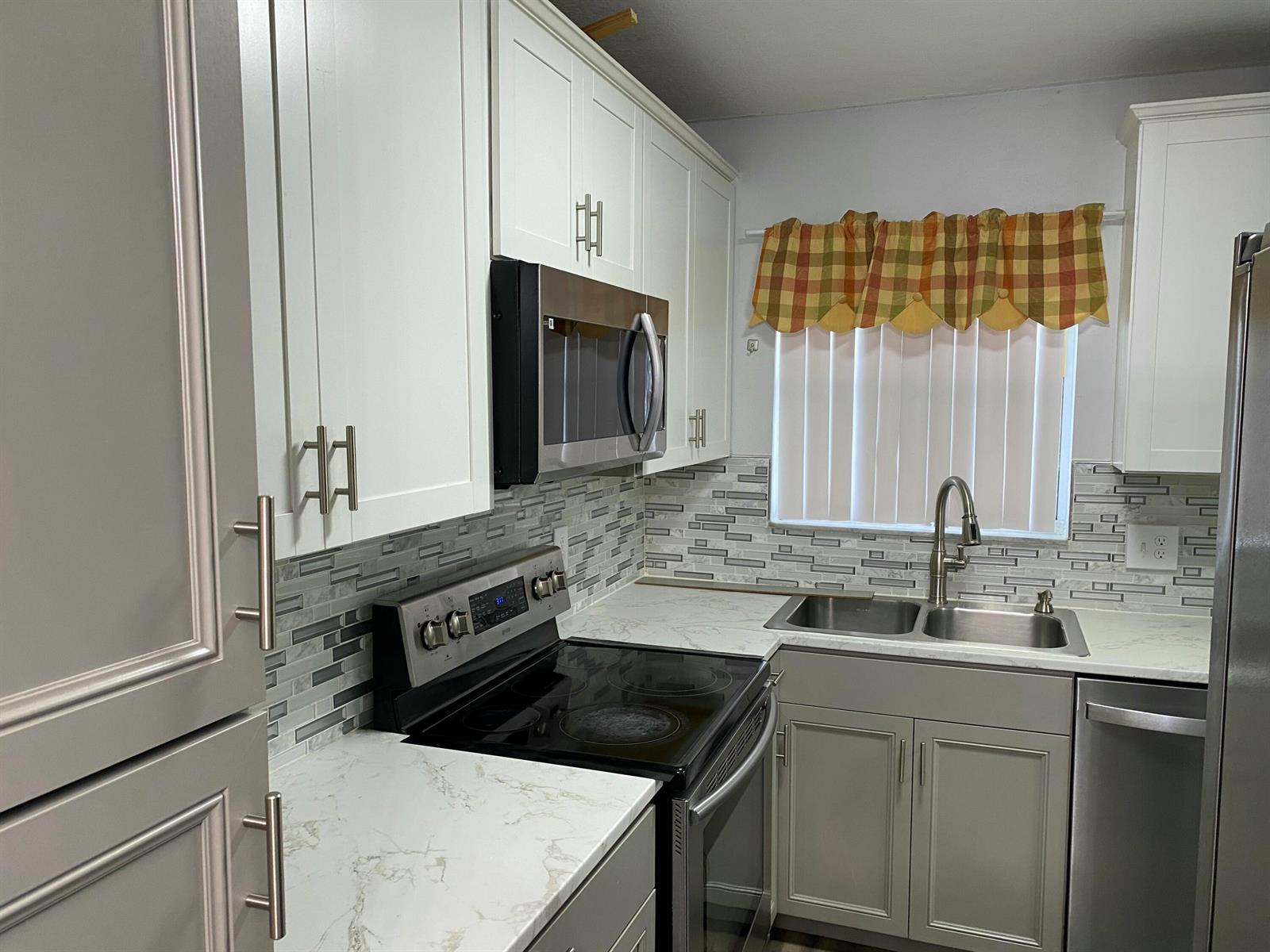 A kitchen features white upper cabinets, gray lower cabinets, stainless steel appliances, and marble countertops — 6890 Royal Palm Boulevard # 209h, Margate FL 33063, MARGATE, FL