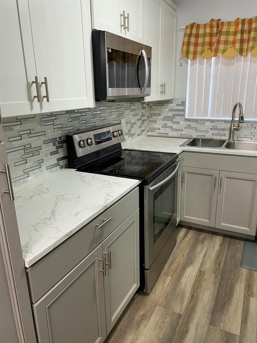 A kitchen features white upper cabinets, gray lower cabinets, marble-look countertops, and a tiled backsplash — 6890 Royal Palm Boulevard # 209h, Margate FL 33063, MARGATE, FL