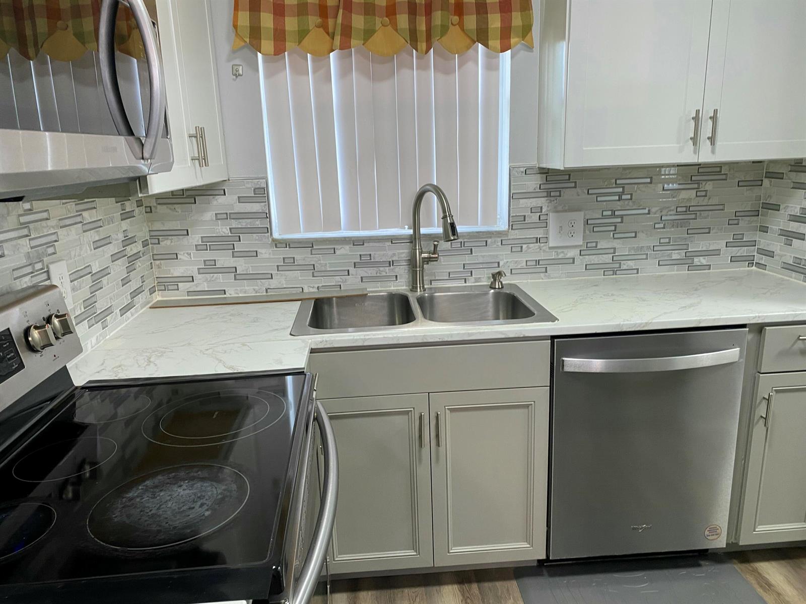 A kitchen features stainless steel appliances, a double-basin sink, white cabinets, and a tiled backsplash — 6890 Royal Palm Boulevard # 209h, Margate FL 33063, MARGATE, FL