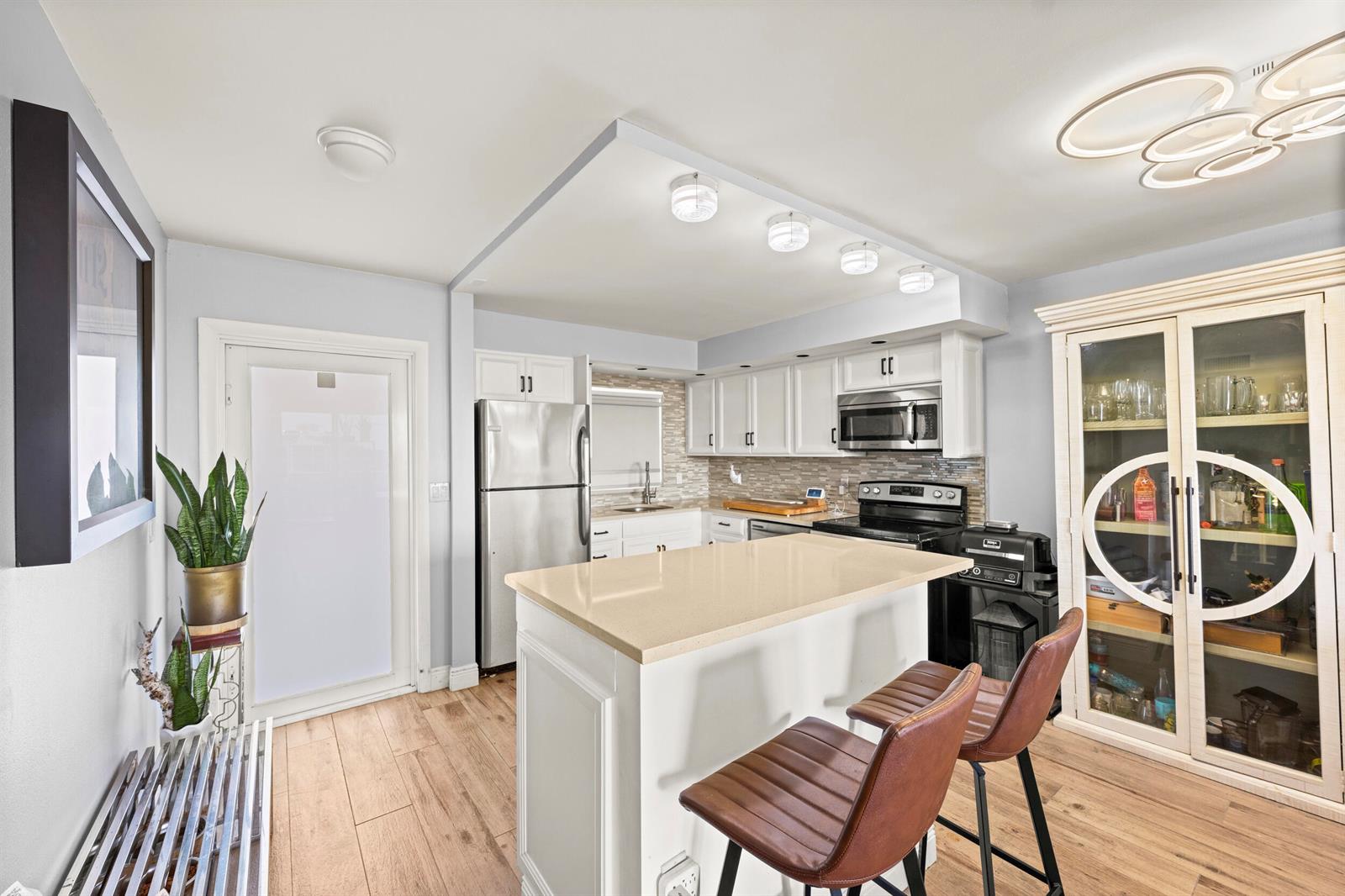 A kitchen features white cabinets, a beige island with bar stools, and light wood flooring — 231 E Lantana Road # 402, Lantana FL 33462, LANTANA, FL