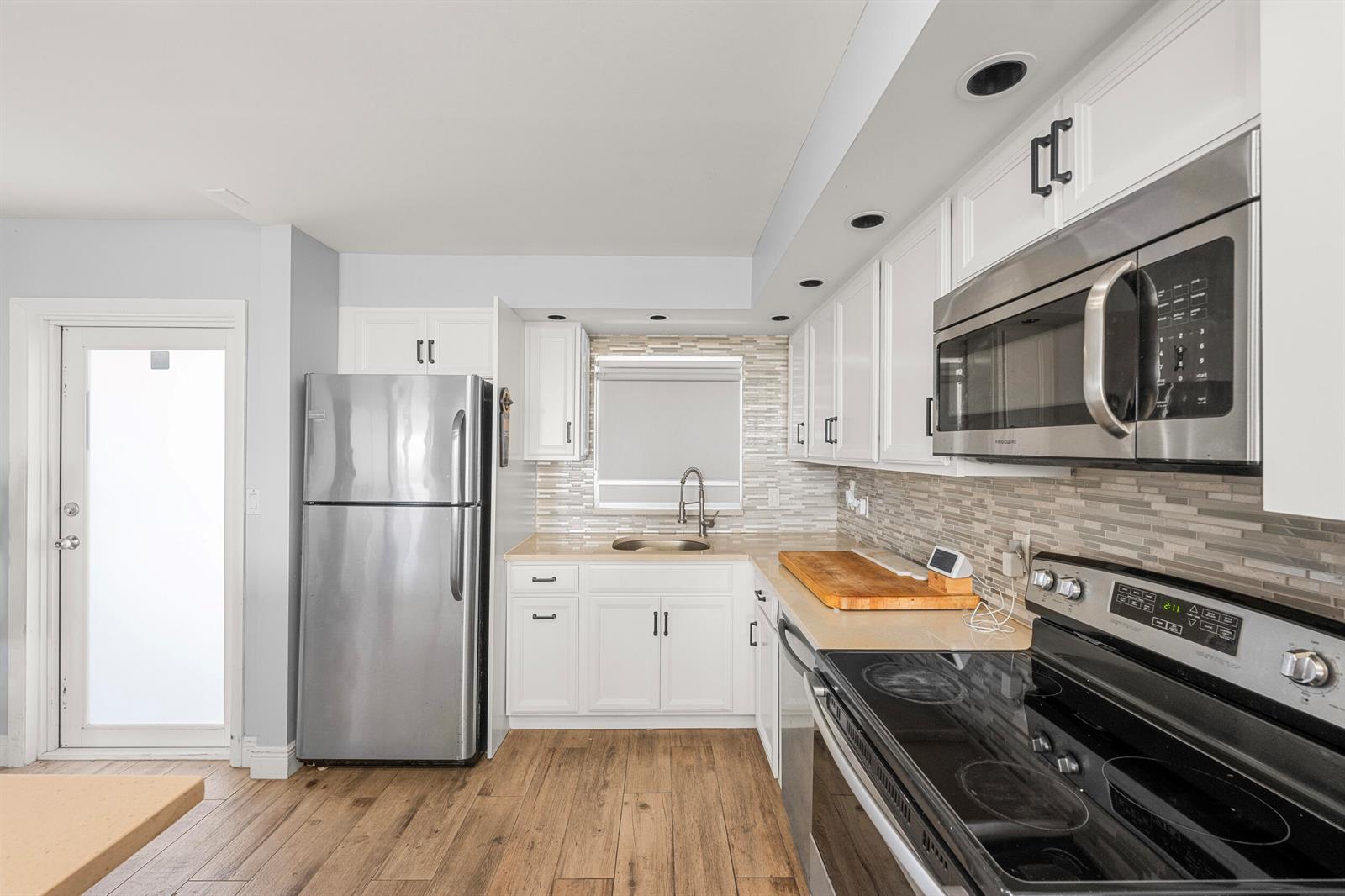 A kitchen features white cabinets, stainless steel appliances, a tiled backsplash, and wood-look flooring — 231 E Lantana Road # 402, Lantana FL 33462, LANTANA, FL