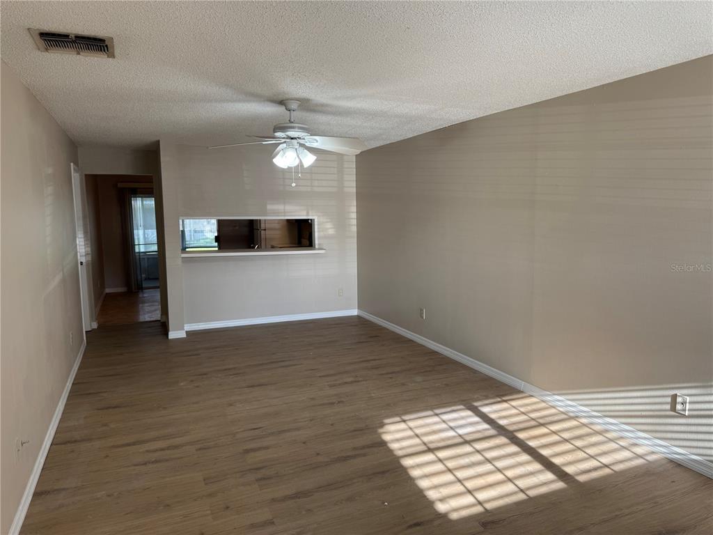 An empty living room features wood-look flooring, a ceiling fan, and a kitchen pass-through window — 1241 HERITAGE LANE, ORLANDO, FL