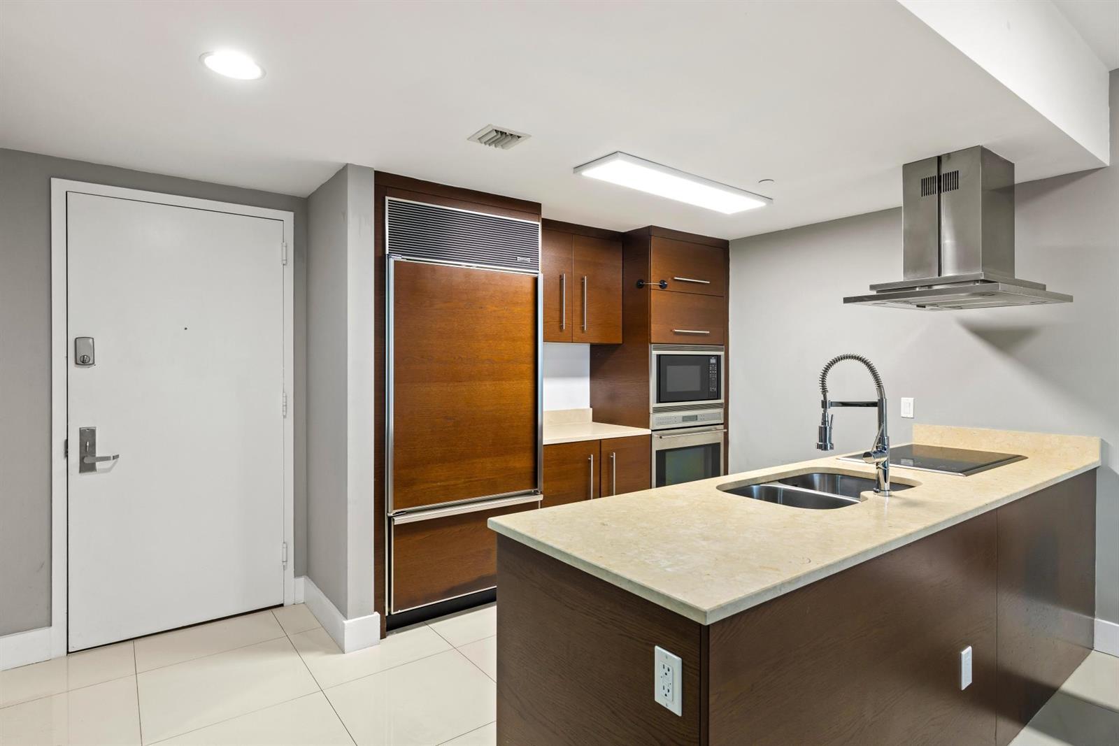 A modern kitchen features dark wood cabinetry, stainless steel appliances, and a stone-topped island — 485 Brickell Avenue # 2506, Miami FL 33131, MIAMI, FL
