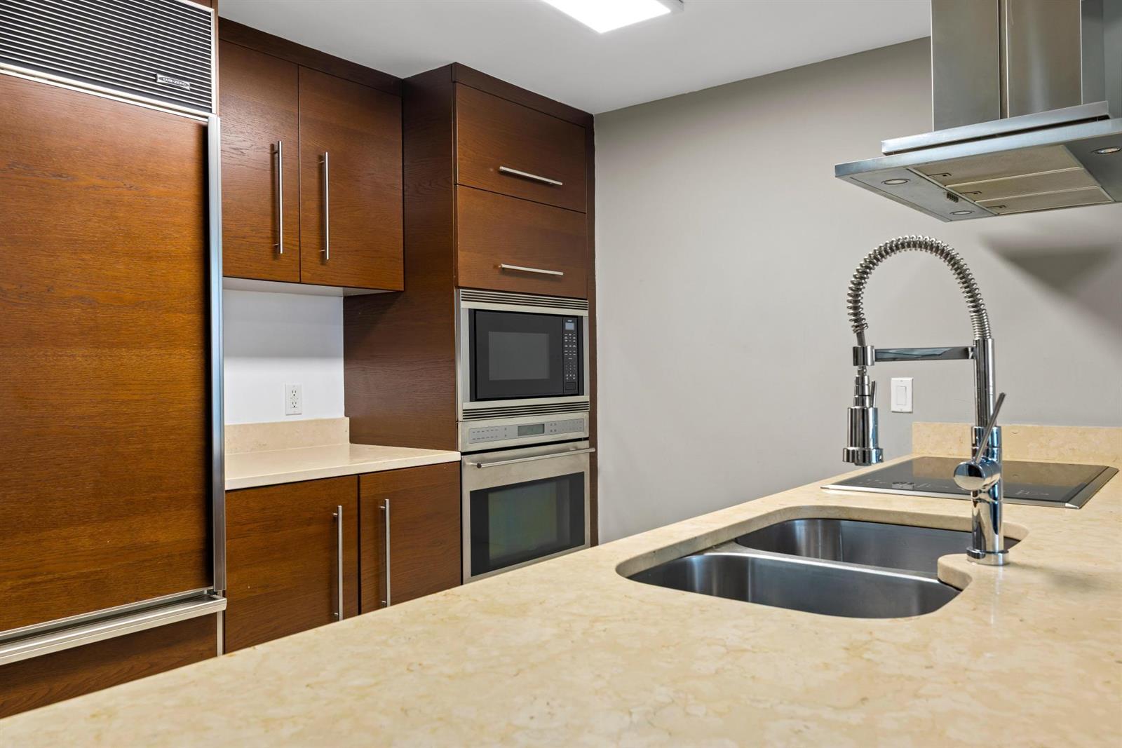 A modern kitchen features wood cabinets, stainless steel appliances, and a light-colored stone countertop — 485 Brickell Avenue # 2506, Miami FL 33131, MIAMI, FL