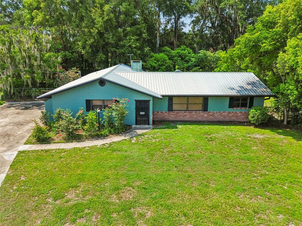 A teal, single-story house with a metal roof and brick accents sits on a grassy lot — 1322 W VOORHIS AVENUE, DELAND, FL