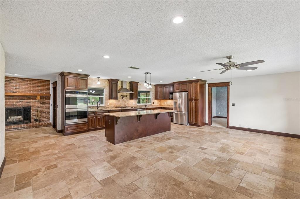 A spacious kitchen features dark wood cabinets, a central island, and stone tile flooring — 1322 W VOORHIS AVENUE, DELAND, FL