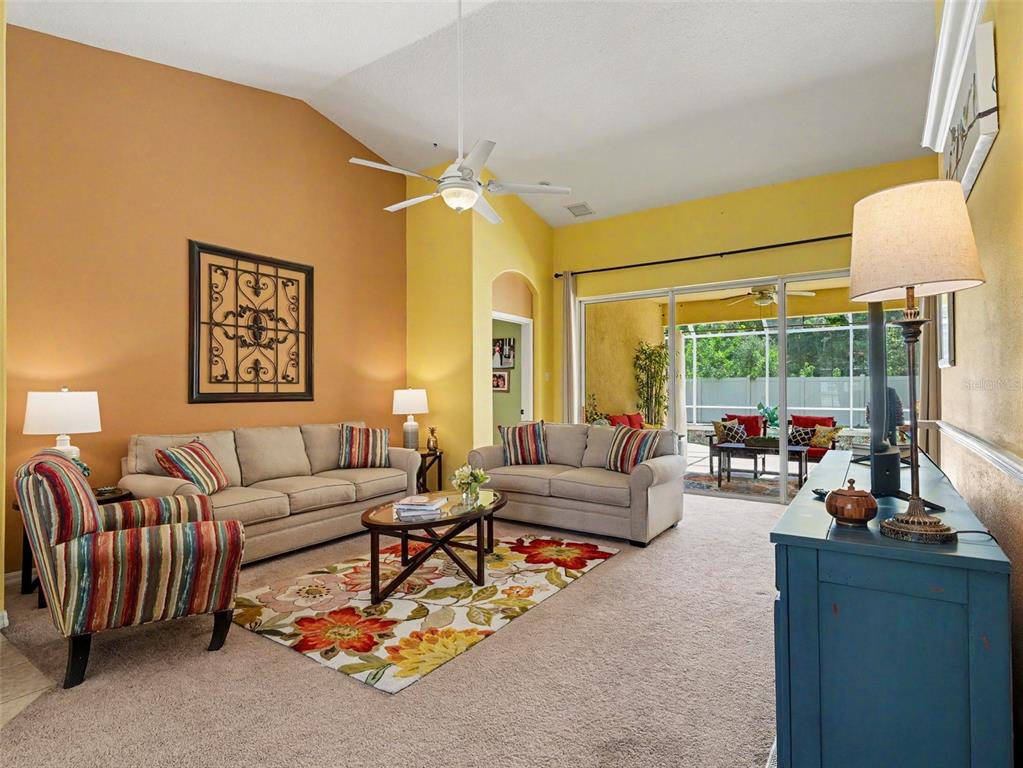 A living room with vaulted ceilings, beige sofas, a colorful rug, and a sliding glass door — 11567 57TH STREET CIRCLE E, PARRISH, FL