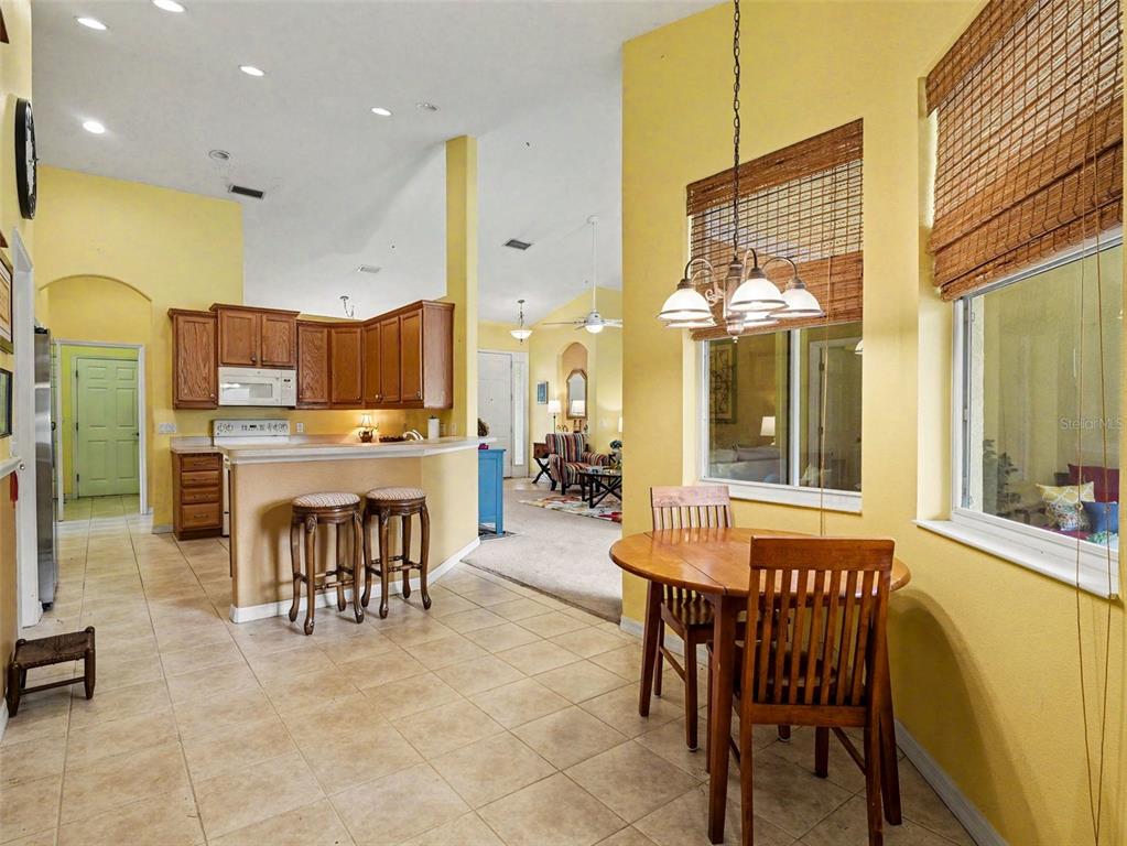 A kitchen with wooden cabinets and a breakfast bar overlooks a dining area and living room — 11567 57TH STREET CIRCLE E, PARRISH, FL