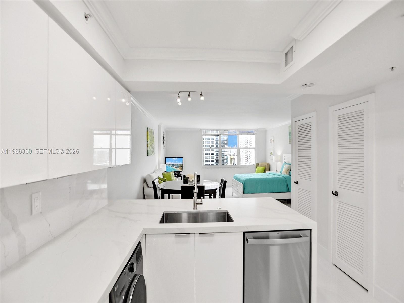 A white kitchen with a stainless steel sink overlooks an open-concept living and bedroom area — 2501 S Ocean Dr, Hollywood FL 33019, HOLLYWOOD, FL