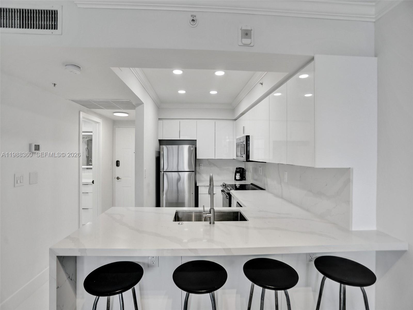 A modern kitchen features white cabinetry, stainless steel appliances, and a marble-topped breakfast bar — 2501 S Ocean Dr, Hollywood FL 33019, HOLLYWOOD, FL