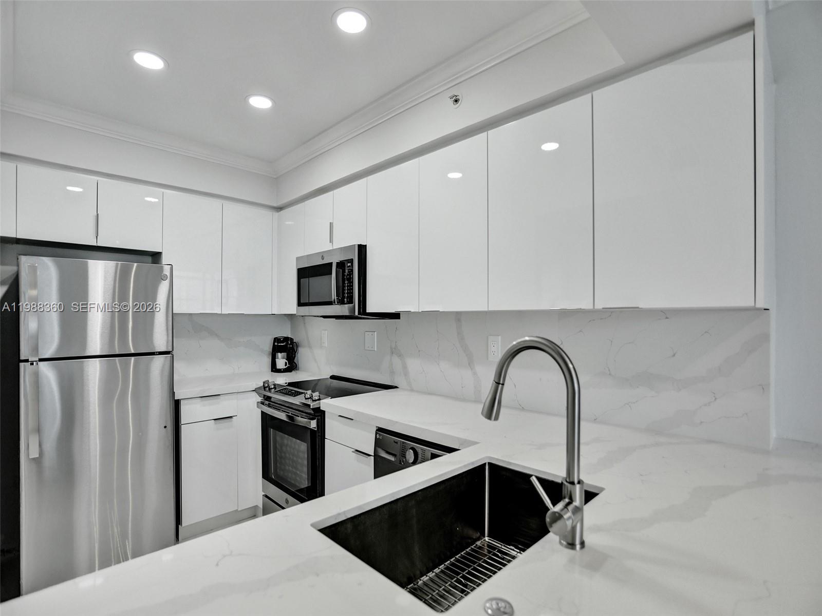A modern kitchen features white cabinets, stainless steel appliances, and marble-patterned countertops and backsplash — 2501 S Ocean Dr, Hollywood FL 33019, HOLLYWOOD, FL