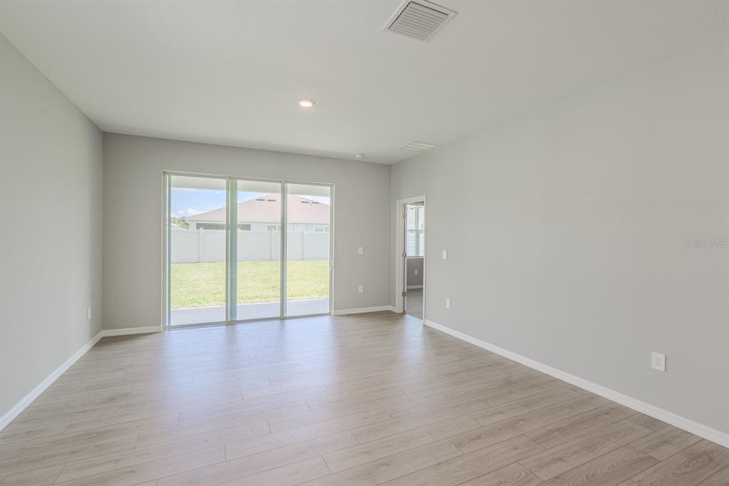 An empty room with light wood-look flooring, gray walls, and sliding glass doors to a yard — 4008 WESTWOOD FIELDS LOOP, PLANT CITY, FL