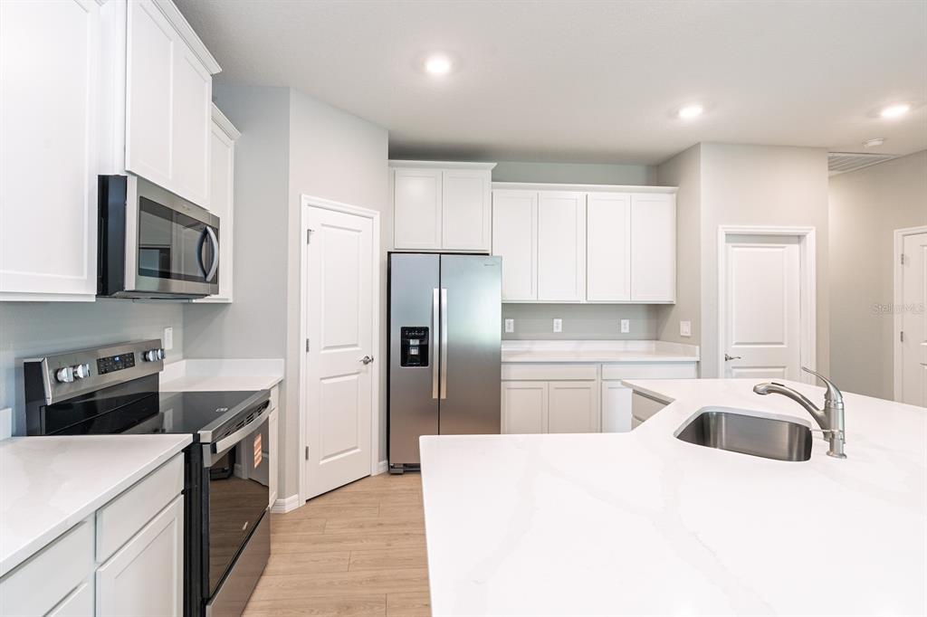 A modern kitchen features white cabinets, stainless steel appliances, and a white quartz island countertop — 4008 WESTWOOD FIELDS LOOP, PLANT CITY, FL