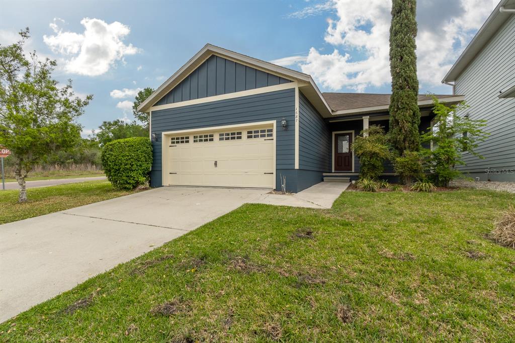 A blue house with a beige garage door and a front porch under a cloudy sky — 1687 NW 120TH WAY, GAINESVILLE, FL