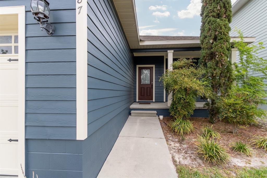 A blue-sided house exterior features a concrete walkway leading to a brown front door — 1687 NW 120TH WAY, GAINESVILLE, FL