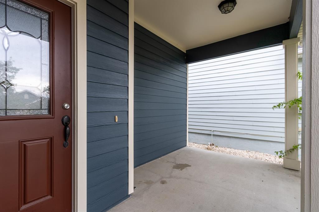 A covered porch with dark blue horizontal siding, a brown front door, and concrete flooring — 1687 NW 120TH WAY, GAINESVILLE, FL