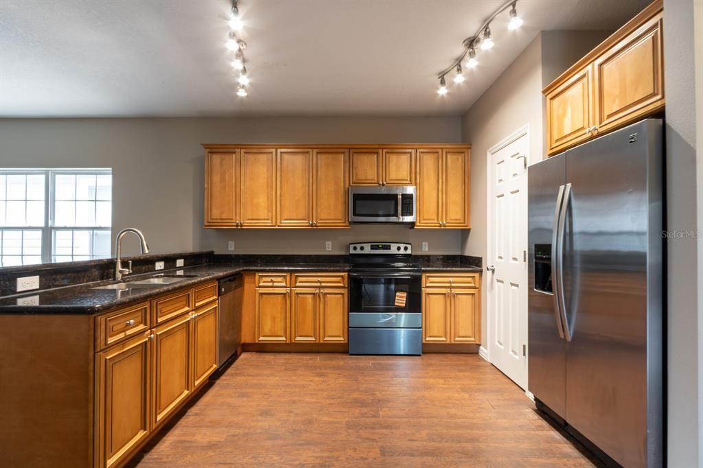 A kitchen features wood cabinets, stainless steel appliances, dark countertops, and track lighting — 1687 NW 120TH WAY, GAINESVILLE, FL