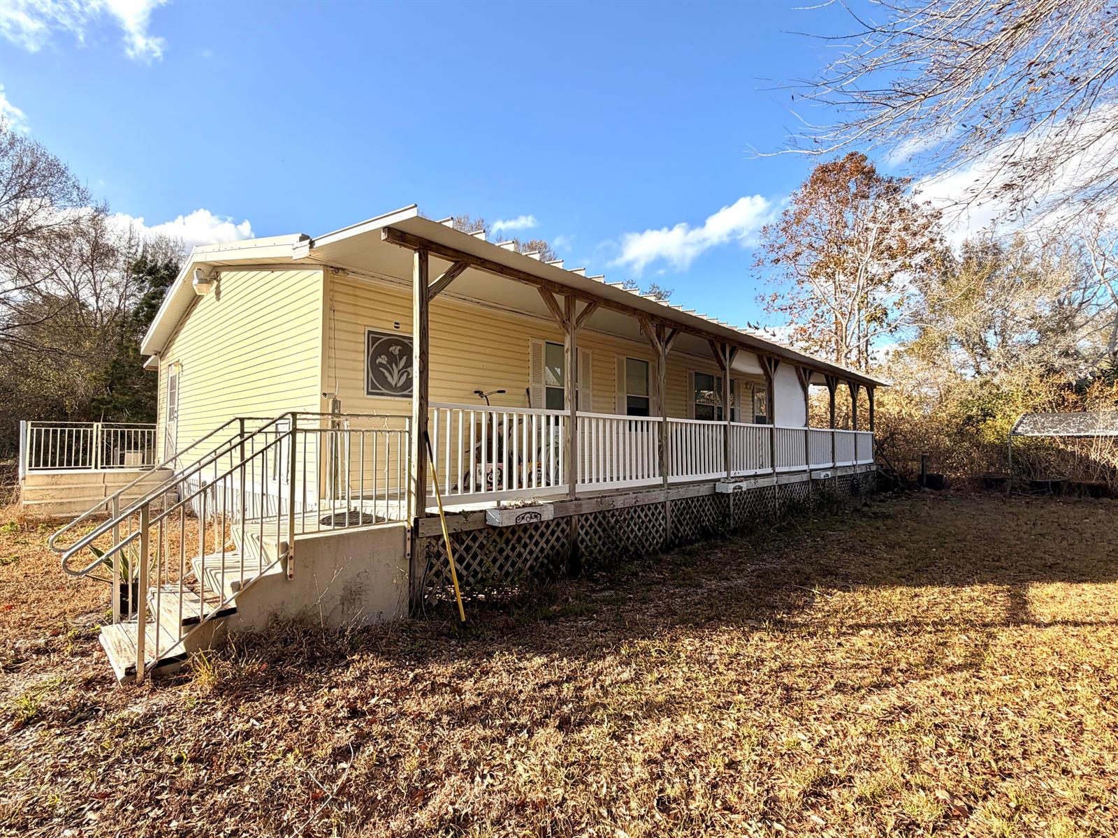 A yellow manufactured home features a long front porch with white railings and stairs — 1907 NE 308th Street, Okeechobee FL 34972, OKEECHOBEE, FL