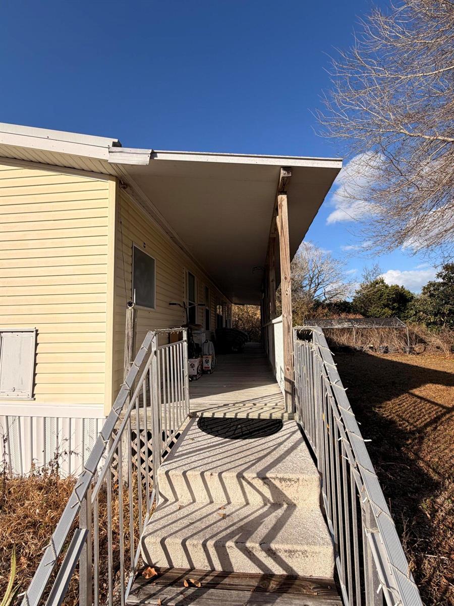 A covered wooden ramp with metal railings leads to the entrance of a yellow mobile home — 1907 NE 308th Street, Okeechobee FL 34972, OKEECHOBEE, FL