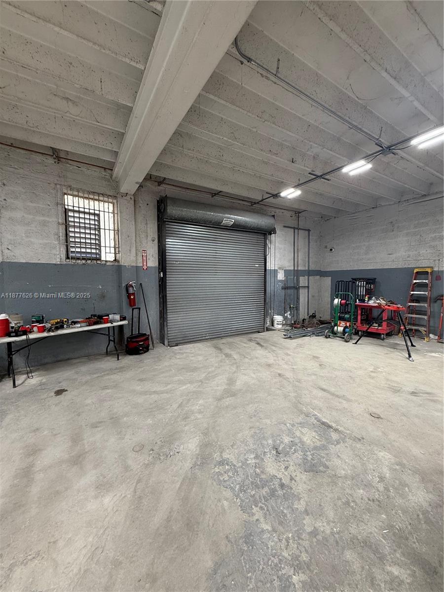 An industrial warehouse space features a concrete floor, exposed ceiling beams, and a roll-up door — 572 NW 72nd St, Miami FL 33150, MIAMI, FL