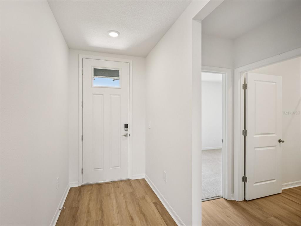 An entryway with light wood-look flooring, a white front door, and an open interior doorway — 1769 FOREST RUN LANE, AUBURNDALE, FL