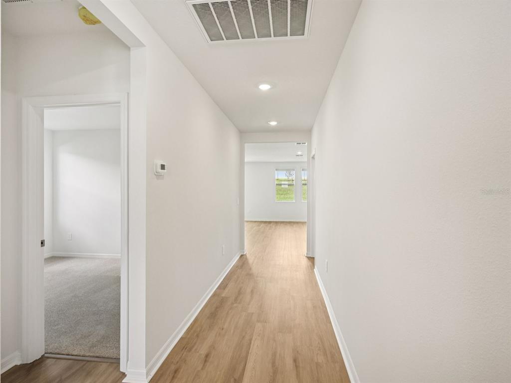 A hallway with light wood-look flooring leads to a room with carpet and a window — 1769 FOREST RUN LANE, AUBURNDALE, FL