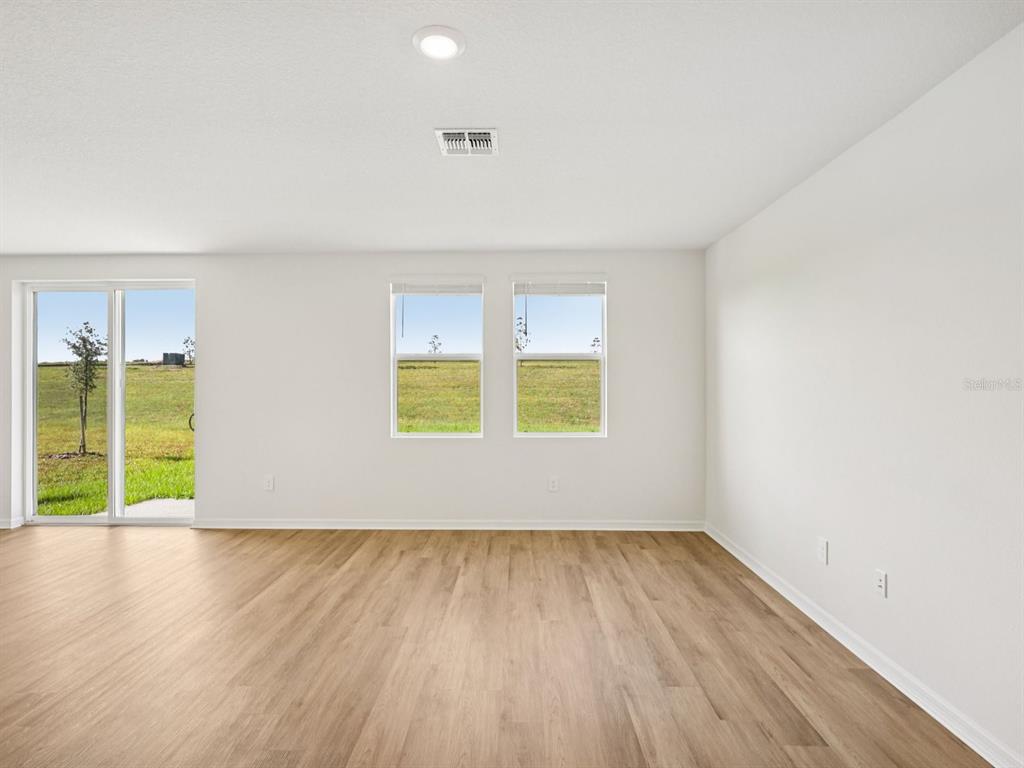 An empty room with light wood-look flooring, white walls, two windows, and a sliding glass door — 1769 FOREST RUN LANE, AUBURNDALE, FL
