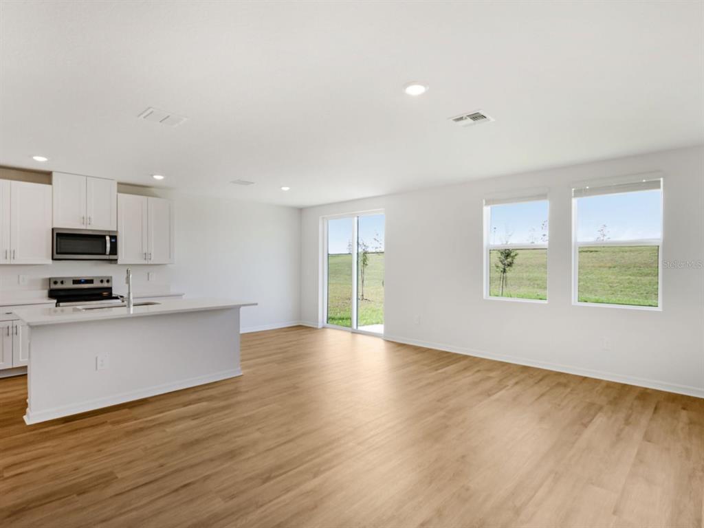 A bright, open-concept kitchen and living area featuring white cabinets, an island, and wood flooring — 1769 FOREST RUN LANE, AUBURNDALE, FL