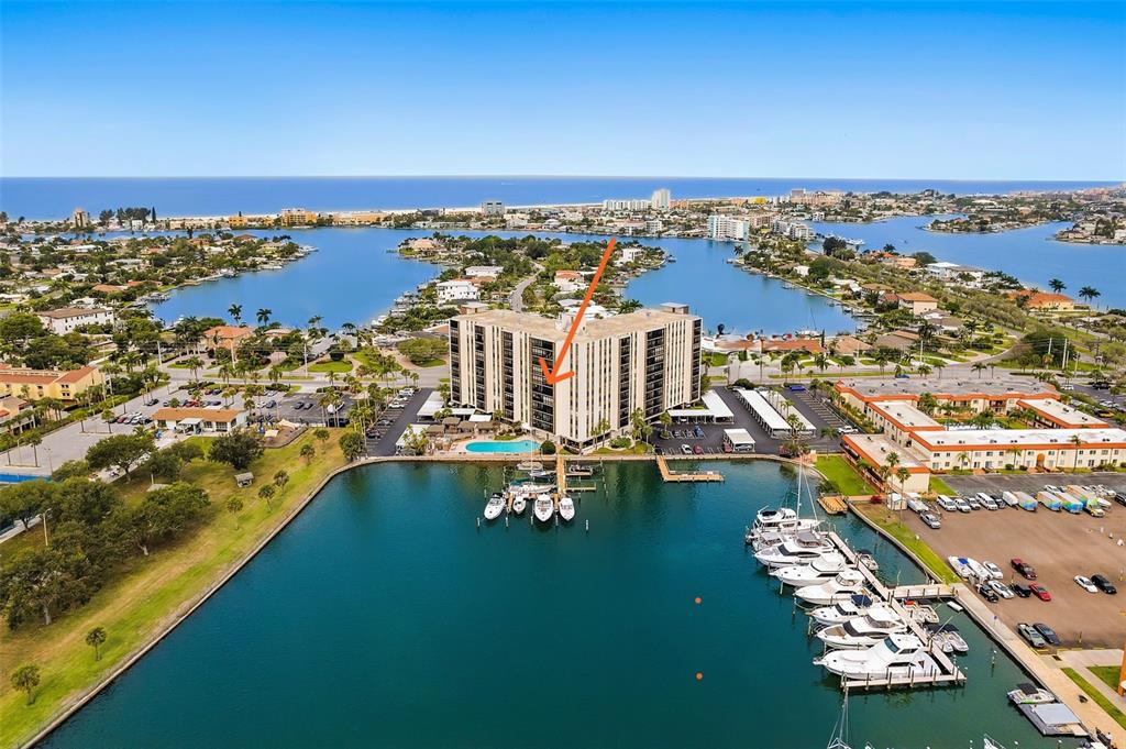 An aerial view shows a multi-story apartment building situated on a waterfront with a marina — 10355 PARADISE BOULEVARD UNIT 608, TREASURE ISLAND, FL