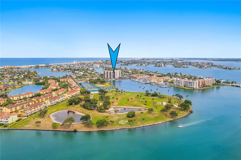 An aerial view shows a high-rise condominium building situated on a waterfront peninsula — 10355 PARADISE BOULEVARD UNIT 608, TREASURE ISLAND, FL