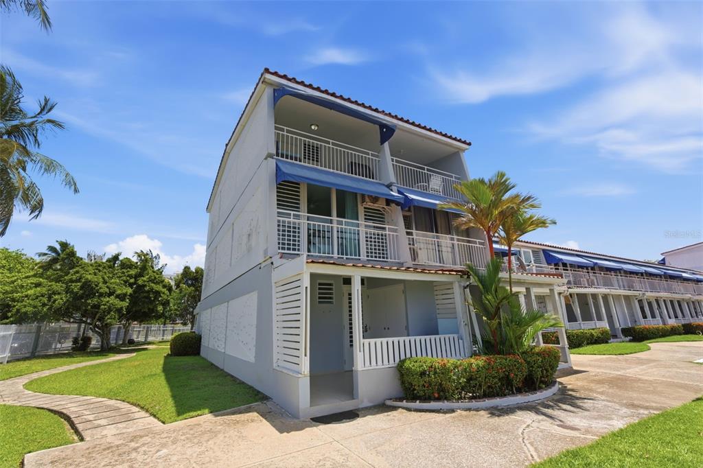 A three-story building with balconies and blue awnings sits on a grassy lawn — Villas de Playa II DORADO DEL MAR UNIT BB-2, DORADO, PR