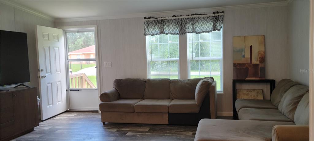 A living room features light wood-look flooring, a brown sofa, and a door leading outside — 11625 NW 20TH STREET, OCALA, FL
