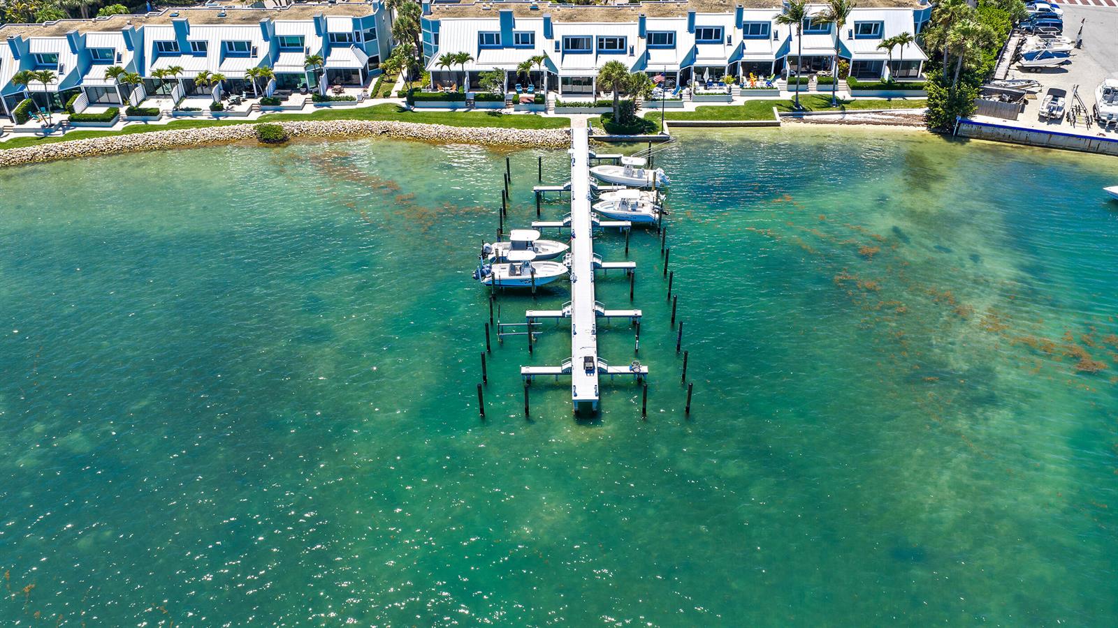 An aerial view of a long boat dock extending into clear water from waterfront townhomes — 19932 Scrimshaw Way, Jupiter FL 33469, JUPITER, FL