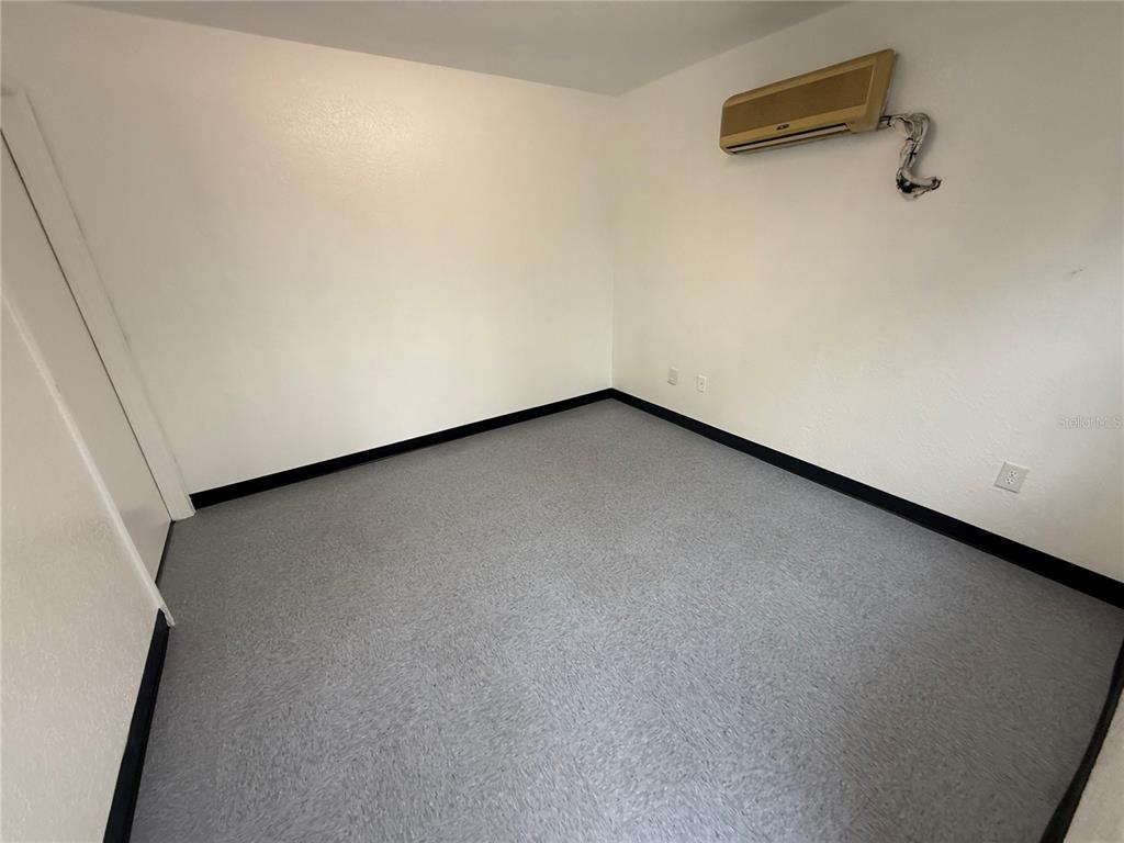 An empty room with white walls, gray flooring, black baseboards, and a wall-mounted air conditioner — 4534 NE 35TH STREET UNIT 7, OCALA, FL
