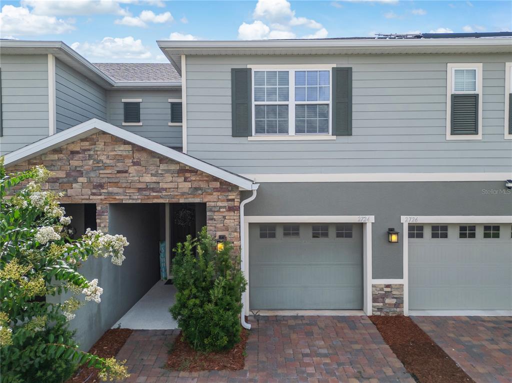 A two-story townhouse exterior features gray horizontal siding, stone veneer accents, and a paved driveway — 2724 PLEASANT CYPRESS CIRCLE, KISSIMMEE, FL