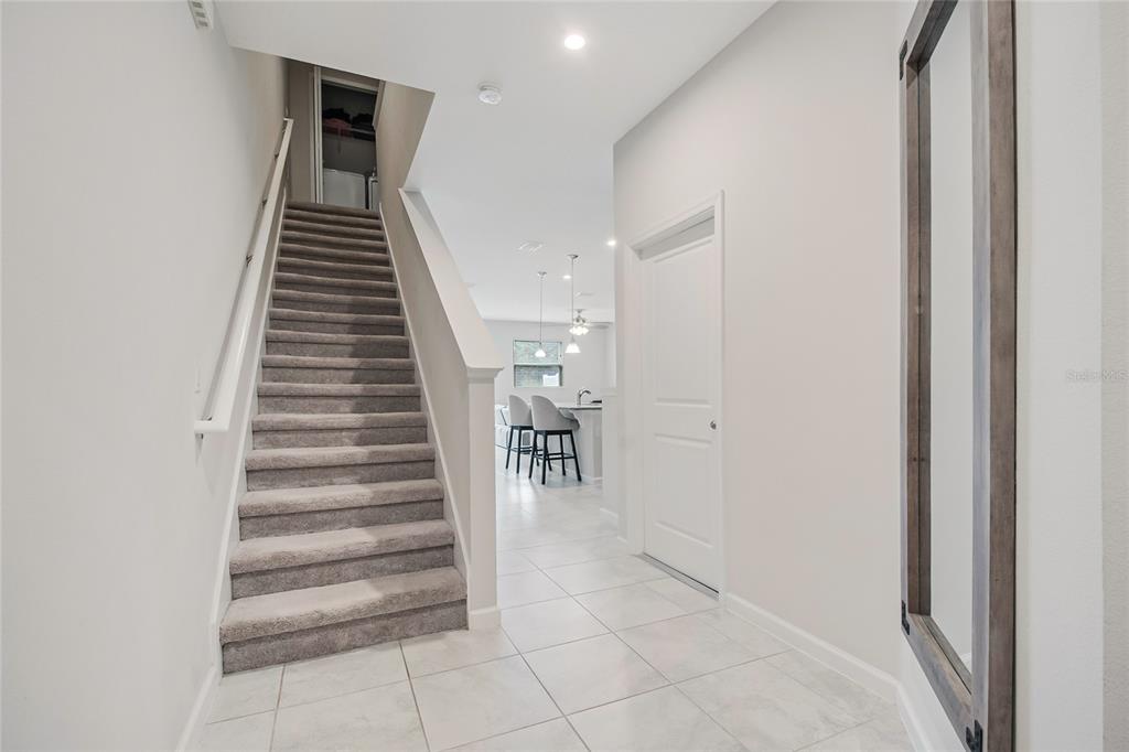 A carpeted staircase leads upstairs next to a tiled entryway and a closed white door — 2724 PLEASANT CYPRESS CIRCLE, KISSIMMEE, FL
