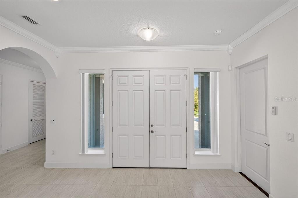 A bright entryway features white double doors flanked by tall windows and light tile flooring — 6808 FORKMEAD LANE, PORT ORANGE, FL