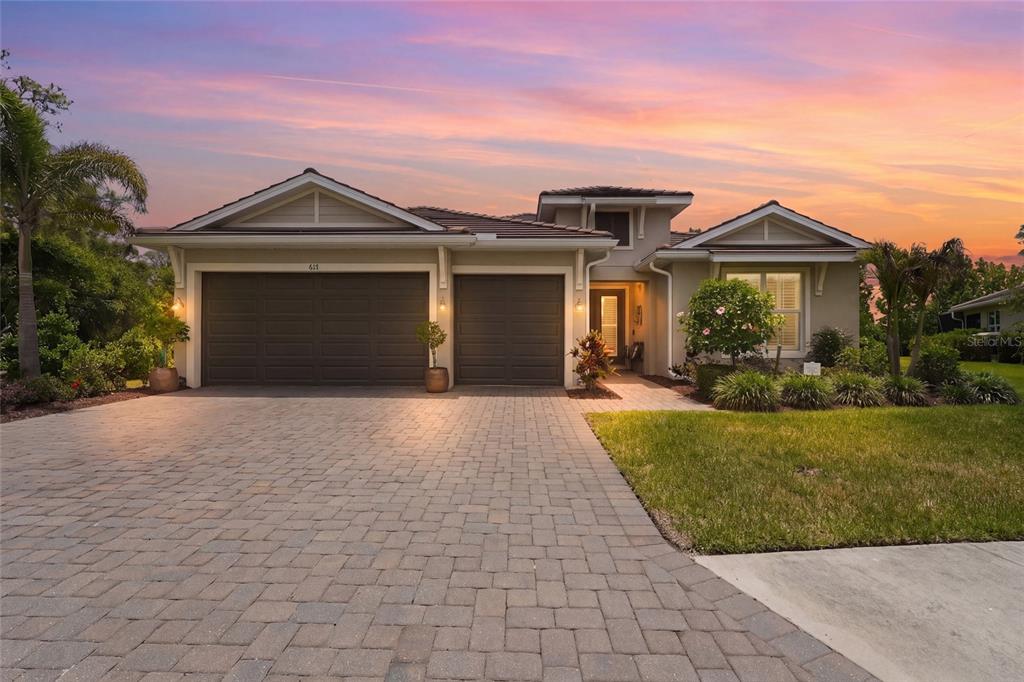 A single-story house with a paved driveway, three-car garage, and landscaped front yard at sunset — 617 MISTIFLOWER CIRCLE, NOKOMIS, FL