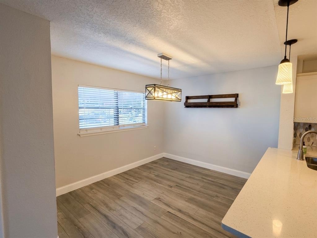 A dining area features wood-look flooring, a rectangular chandelier, and a wall-mounted wooden shelf — 150 KILLARNEY BAY COURT UNIT 5-5, WINTER PARK, FL