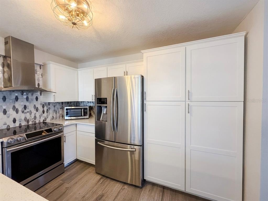 A kitchen features white cabinetry, stainless steel appliances, and a geometric patterned backsplash — 150 KILLARNEY BAY COURT UNIT 5-5, WINTER PARK, FL