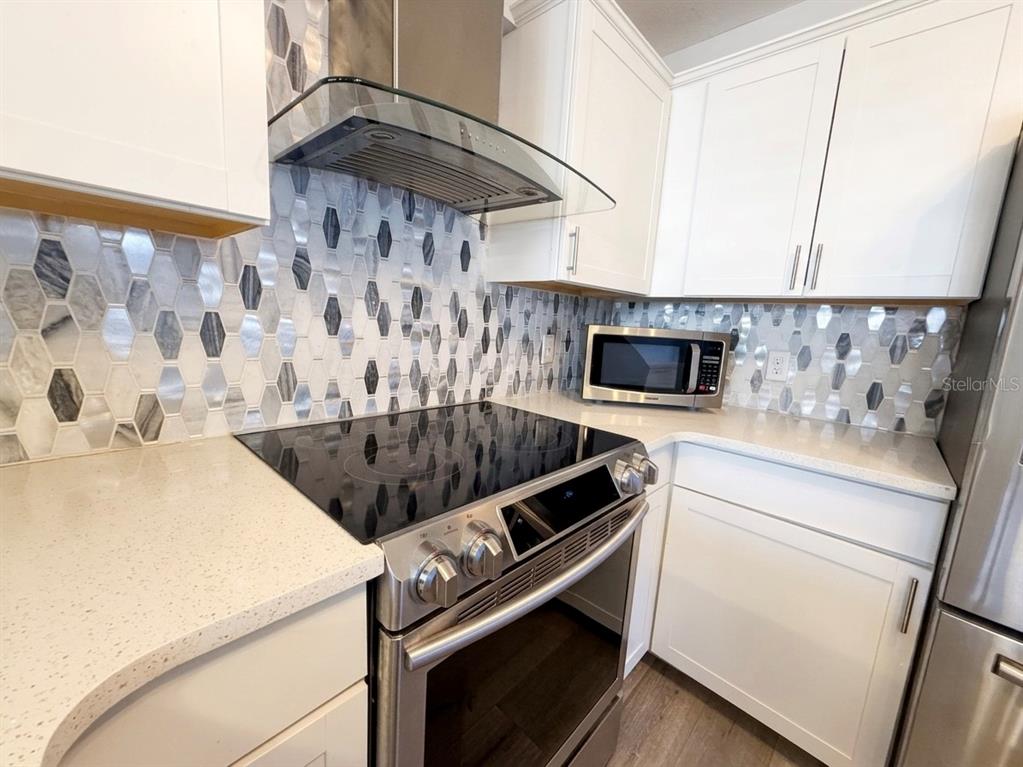 A kitchen features white cabinets, a stainless steel range, and a patterned hexagonal tile backsplash — 150 KILLARNEY BAY COURT UNIT 5-5, WINTER PARK, FL