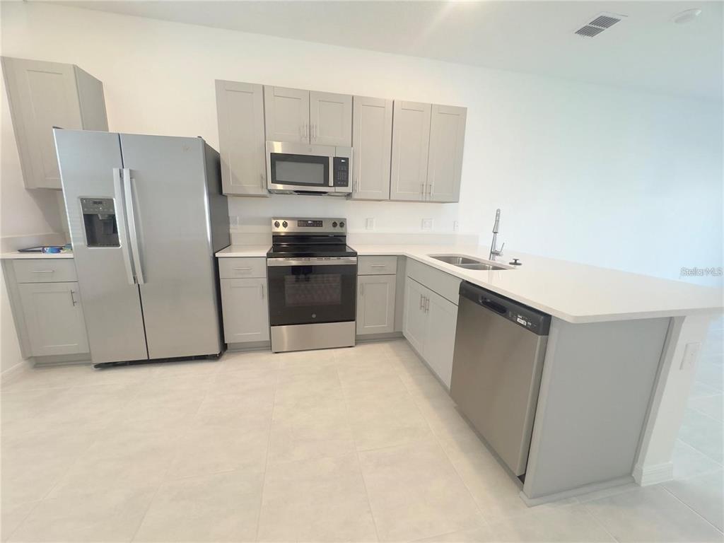 A kitchen features light gray cabinets, stainless steel appliances, and white countertops — 2852 SKYLINE LOOP, KISSIMMEE, FL