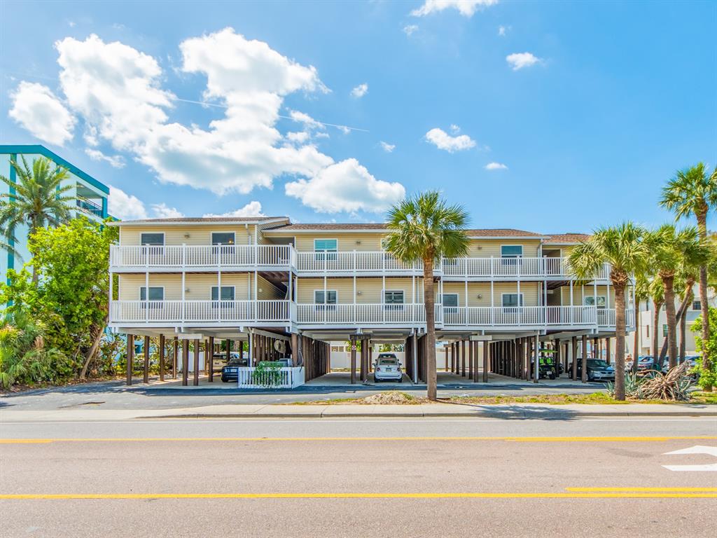 A three-story yellow apartment building on stilts with white railings and palm trees in front — 2406 GULF BOULEVARD UNIT 204, INDIAN ROCKS BEACH, FL