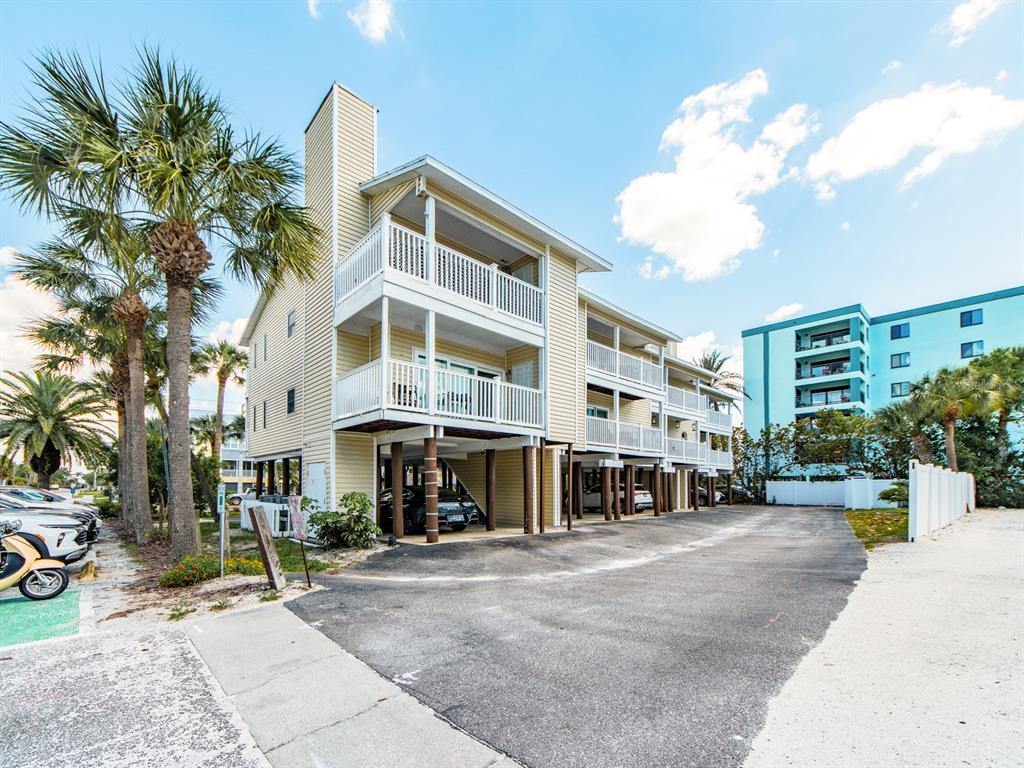An exterior view of a multi-story yellow building on stilts with balconies and parking underneath — 2406 GULF BOULEVARD UNIT 204, INDIAN ROCKS BEACH, FL