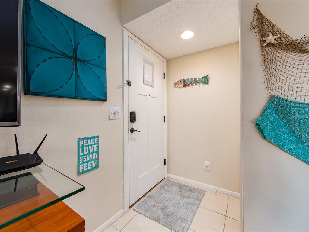 An entryway features a white door, tiled floor, and beach-themed wall decor — 2406 GULF BOULEVARD UNIT 204, INDIAN ROCKS BEACH, FL