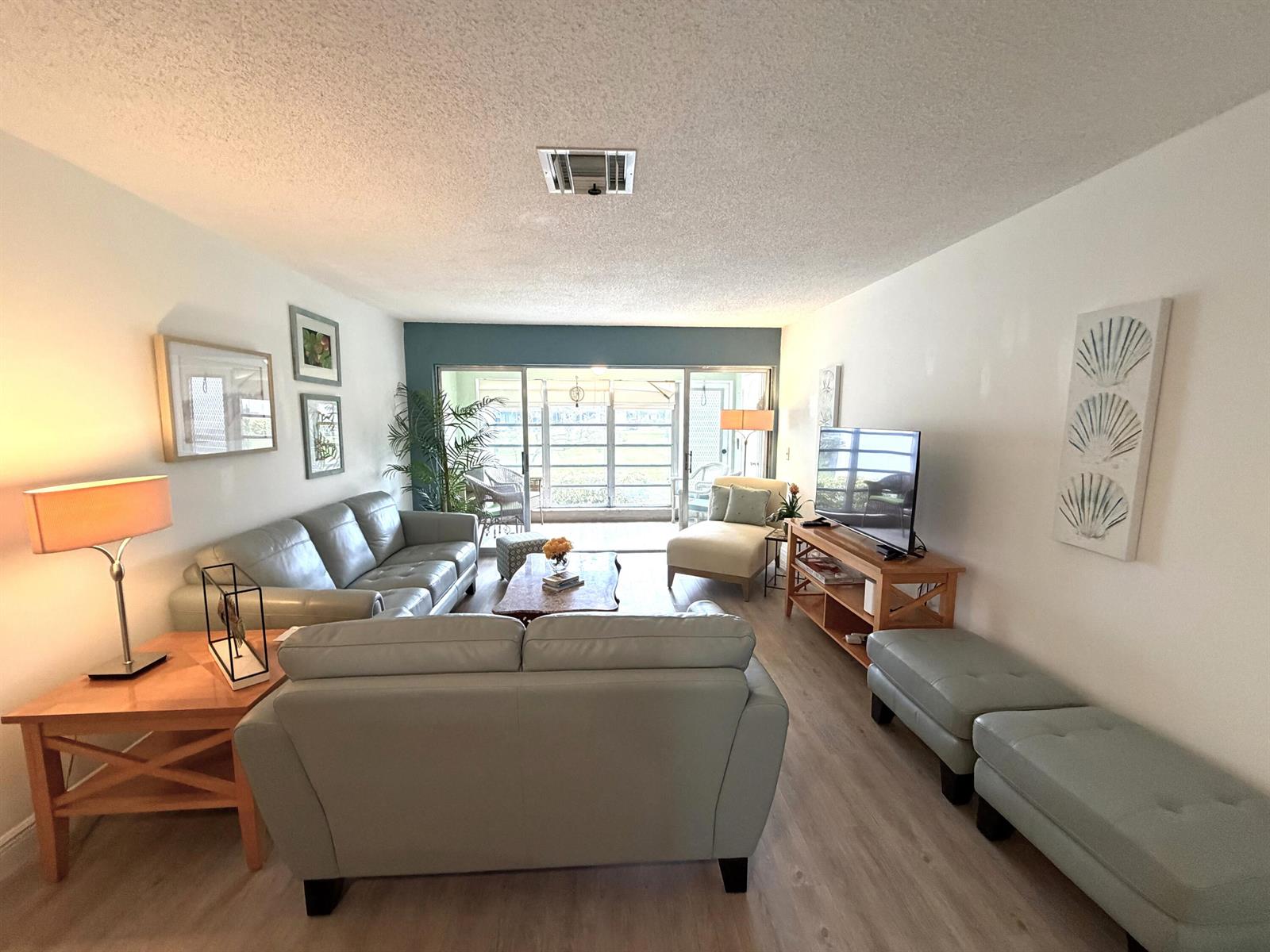 A living room features light-colored leather sofas, a wooden media console, and sliding glass doors — 2520 Pansey Lane # D, Delray Beach FL 33445, DELRAY BEACH, FL
