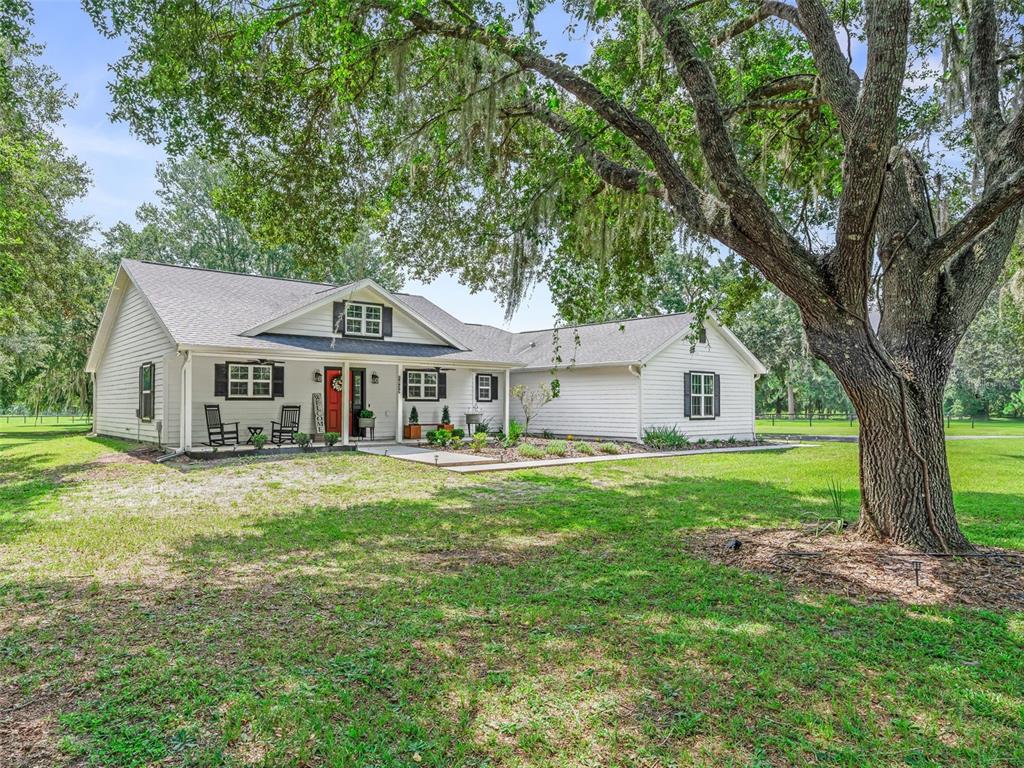 A covered porch with a rocking chair overlooks a grassy yard with large oak trees — 1539 SE 34TH WAY, SUMTERVILLE, FL