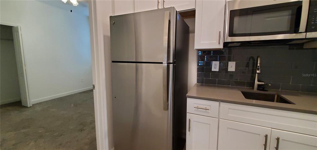A kitchen features a stainless steel refrigerator, white cabinets, and a dark tile backsplash — 1743 GOOD NEIGHBOR LOOP, KISSIMMEE, FL